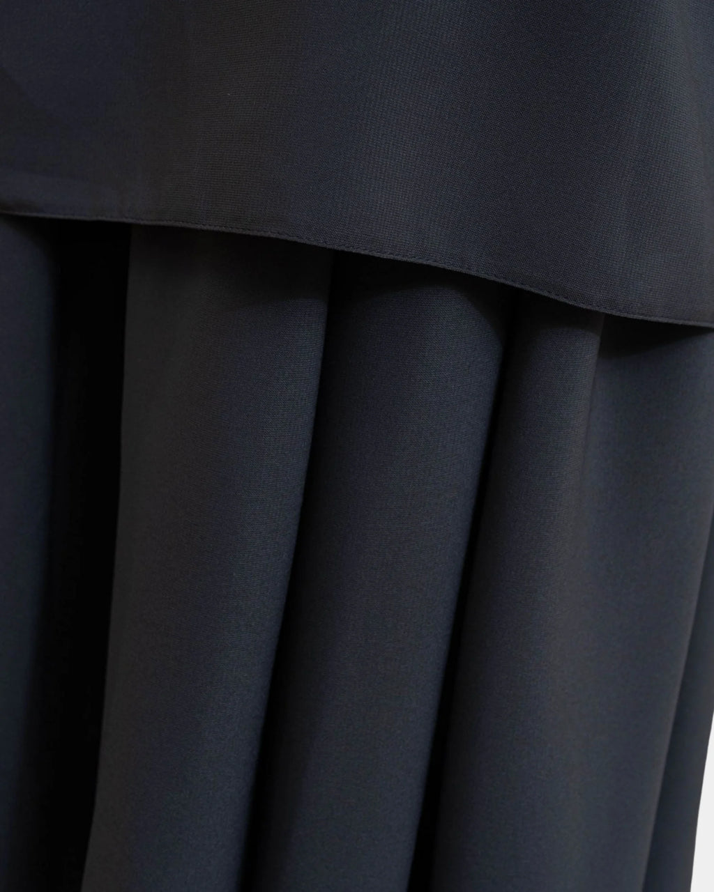 Ourlet du khimar gris foncé retombant sur la jupe assortie, finition surpiquée
