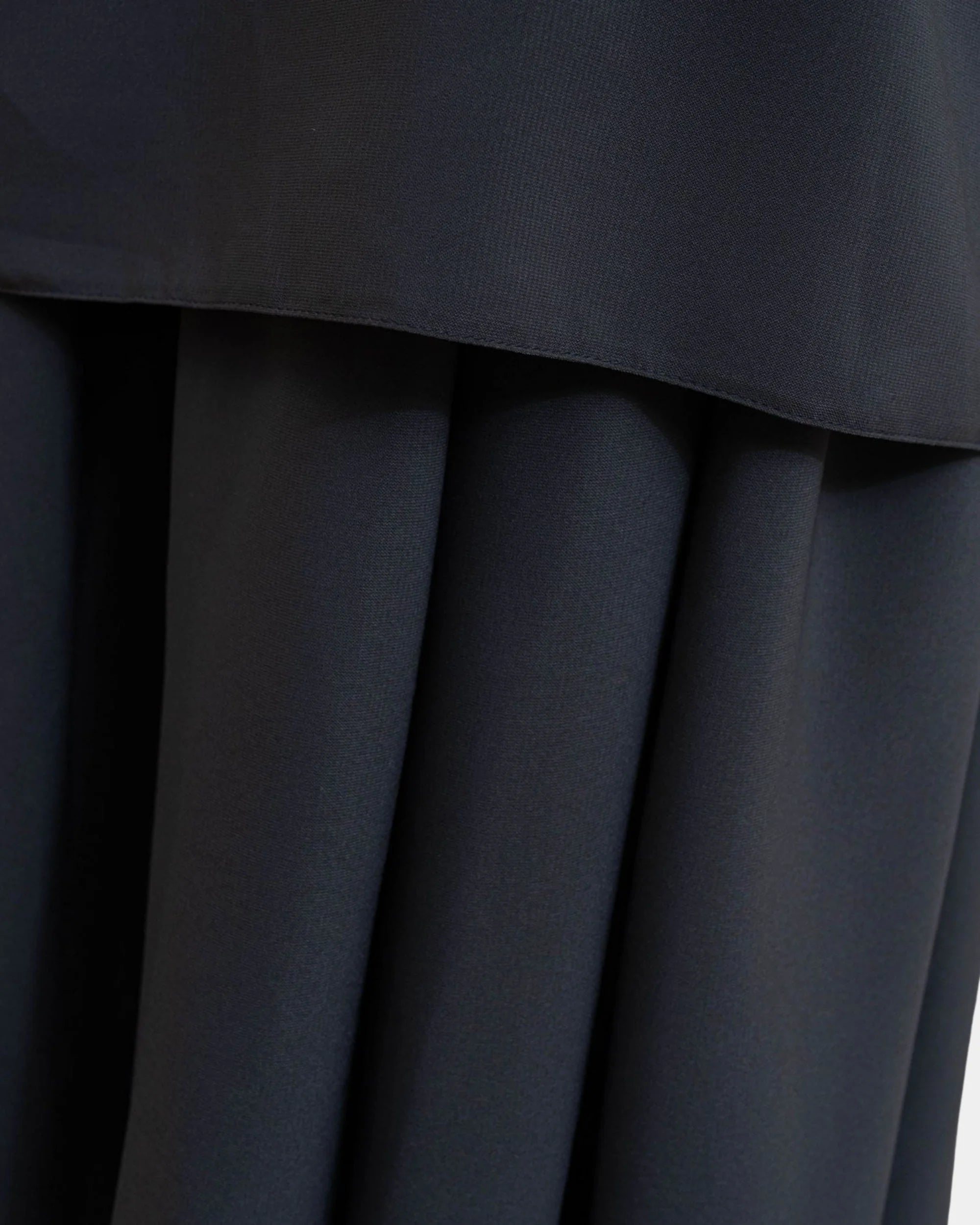 Ourlet du khimar gris foncé retombant sur la jupe assortie, finition surpiquée